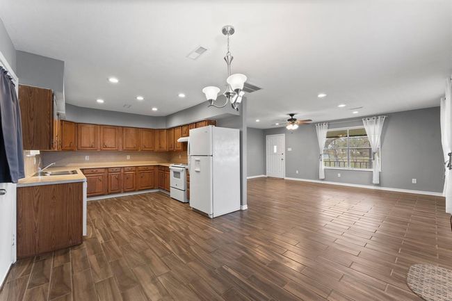 This spacious open-concept area features a kitchen with ample wooden cabinetry, modern lighting, and appliances. The living space has large windows, providing a bright and welcoming atmosphere. | Image 15