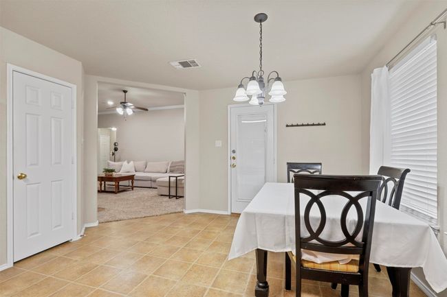 Dining space with light tile patterned floors, ceiling fan with notable chandelier, visible vents, and baseboards | Image 13