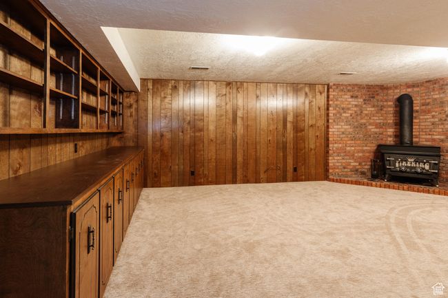 Finished basement featuring a textured ceiling, wood walls, a wood stove, and light carpet | Image 19