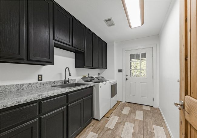 Laundry area featuring washing machine and dryer, cabinet space, and light wood look tile flooring | Image 20