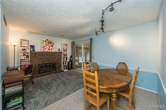 Dining space with carpet flooring, a brick fireplace, a textured ceiling, baseboards, and track lighting | Image 17