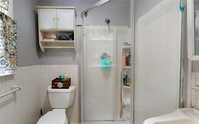 Bathroom with a shower stall, toilet, tile walls, and a wainscoted wall | Image 29