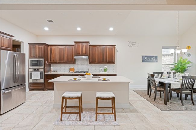 Kitchen featuring appliances with stainless steel finishes, backsplash, light countertops, light tile patterned flooring, and a kitchen island with sink | Image 13