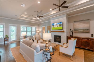 Living room featuring ornamental molding, ceiling fan, a large fireplace, a tray ceiling, and light wood-type flooring | Image 3