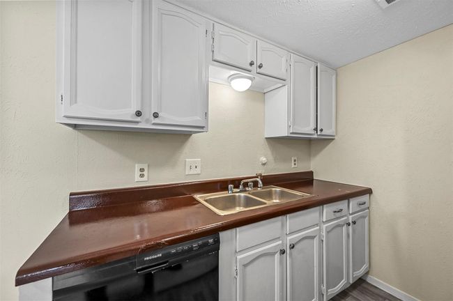 Kitchen with dark countertops, black dishwasher, a textured ceiling, white cabinets, and dark wood finished floors | Image 5