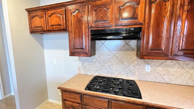 Kitchen with black gas stovetop, under cabinet range hood, backsplash, and light countertops | Image 7