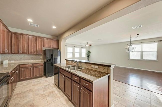 Kitchen with a sink, black appliances, backsplash, a ceiling fan, and an island with sink | Image 7