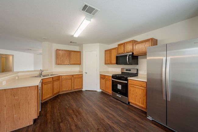 Kitchen with appliances with stainless steel finishes, a sink, dark wood-style flooring, light countertops, and a peninsula | Image 10