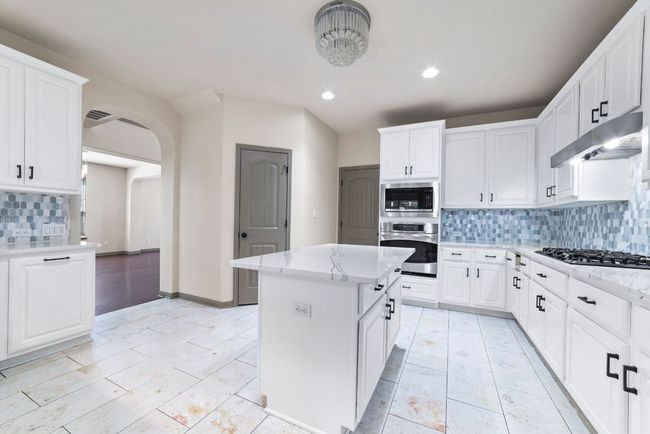 Kitchen featuring appliances with stainless steel finishes, tasteful backsplash, under cabinet range hood, arched walkways, and a kitchen island | Image 16