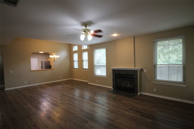 Unfurnished living room featuring a chandelier, ceiling fan, a tiled fireplace, and dark wood-style floors | Image 10