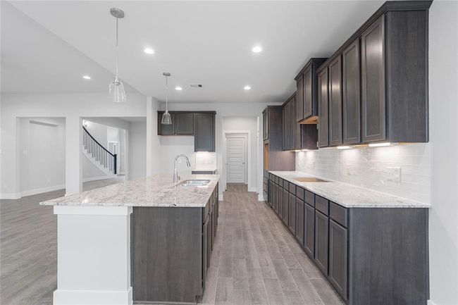 This kitchen is by far any chef’s dream! This spacious kitchen features high ceilings, stained wood cabinets, granite countertops, SS appliances, modern tile backsplash, recessed and pendant lighting, extended counter space, granite kitchen island with space for breakfast bar, and a walk-in pantry all overlooking your huge family room. | Image 7