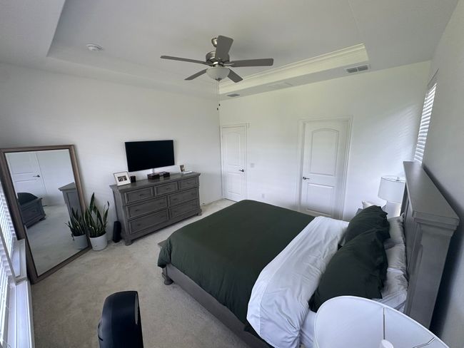 Bedroom featuring light carpet, a raised ceiling, and a ceiling fan | Image 6
