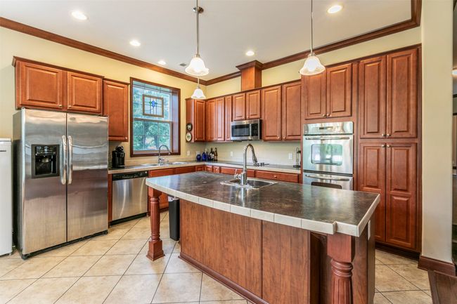 Kitchen featuring light tile patterned flooring, appliances with stainless steel finishes, ornamental molding, and a sink | Image 5