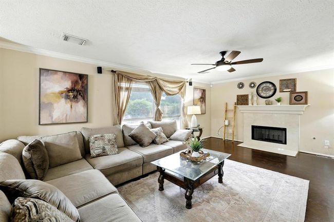 Spacious family room features a classic fireplace, crown molding, and rich wood flooring for a warm and welcoming atmosphere. Large windows provide natural light and backyard views. | Image 9