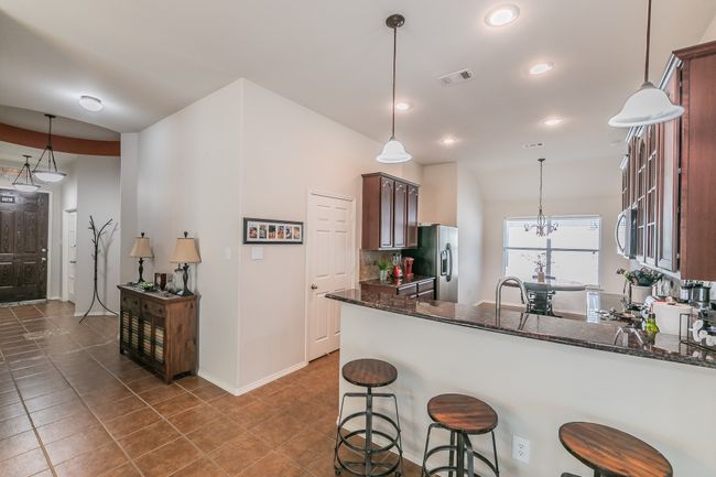 Kitchen featuring visible vents, dark stone counters, a peninsula, a kitchen breakfast bar, and stainless steel appliances | Image 9
