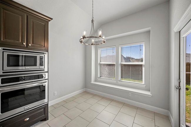 Kitchen featuring light tile patterned floors, an inviting chandelier, lofted ceiling, stainless steel appliances, and dark brown cabinets | Image 14