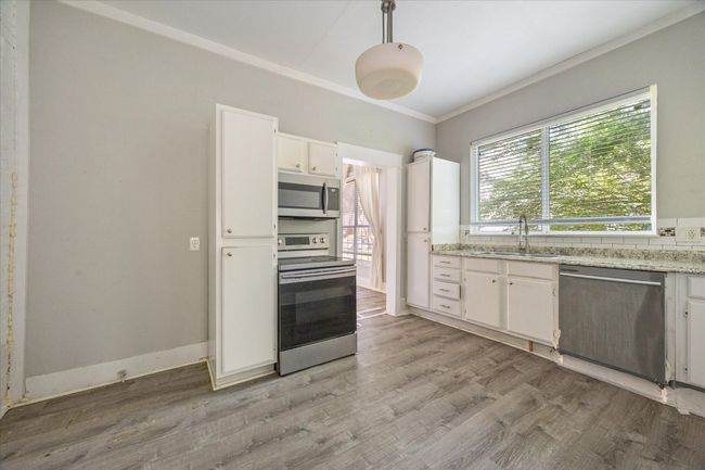 Kitchen featuring appliances with stainless steel finishes, white cabinetry, crown molding, light wood-type flooring, and pendant lighting | Image 9
