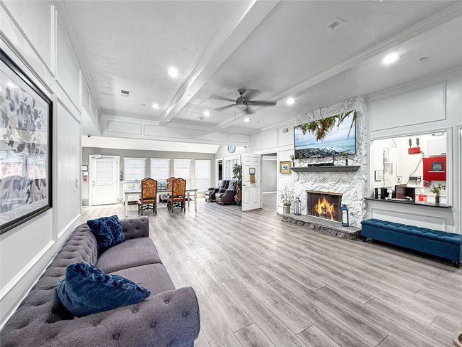 Living room with beamed ceiling, a stone fireplace, ceiling fan, light wood finished floors, and crown molding | Image 5