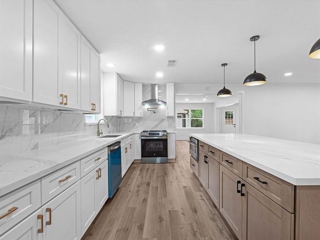 This modern kitchen features sleek white cabinetry, marble countertops, and a spacious island. It includes stainless steel appliances, wood flooring, and stylish pendant lighting, creating a bright and inviting space perfect for cooking and entertaining. | Image 12