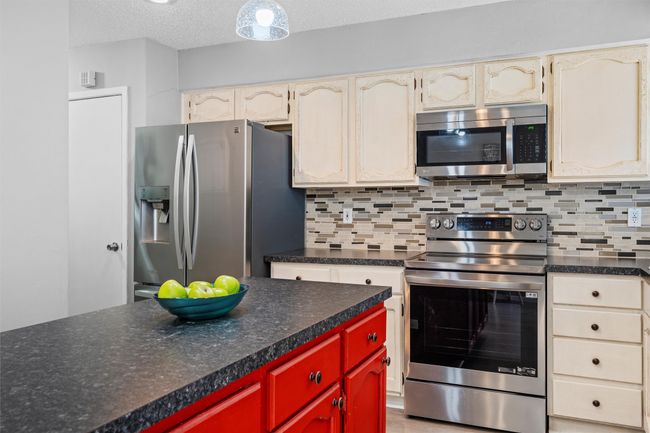 Kitchen with dark countertops, tasteful backsplash, appliances with stainless steel finishes | Image 7