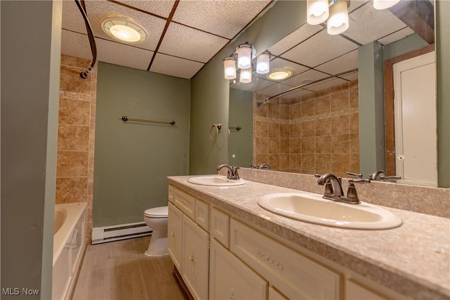 Bathroom featuring a baseboard heating unit, a paneled ceiling, toilet, double vanity, and wood finished floors | Image 13