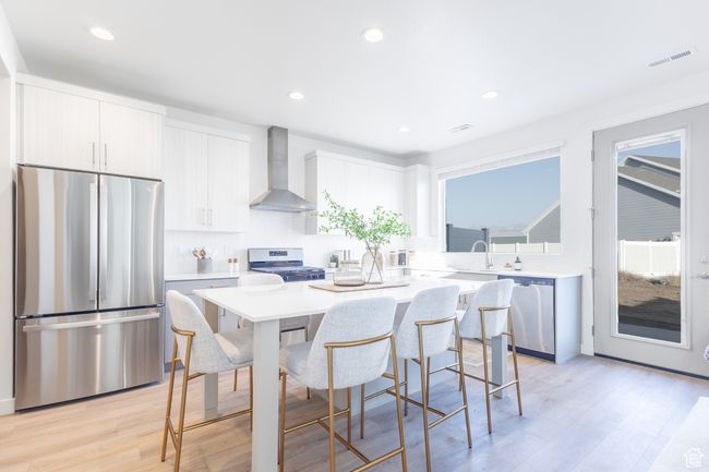 Kitchen with stainless steel appliances, wall chimney range hood, a center island, a kitchen bar, and light countertops | Image 7