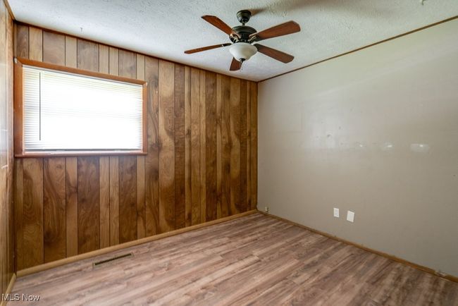 Empty room featuring wood finished floors, wooden walls, a ceiling fan, a textured ceiling, and baseboards | Image 28