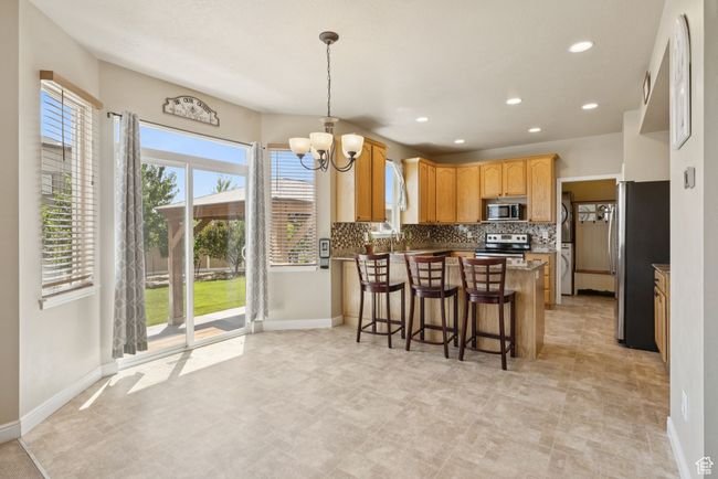 Kitchen with appliances with stainless steel finishes, a peninsula, a chandelier, tasteful backsplash, and recessed lighting | Image 12