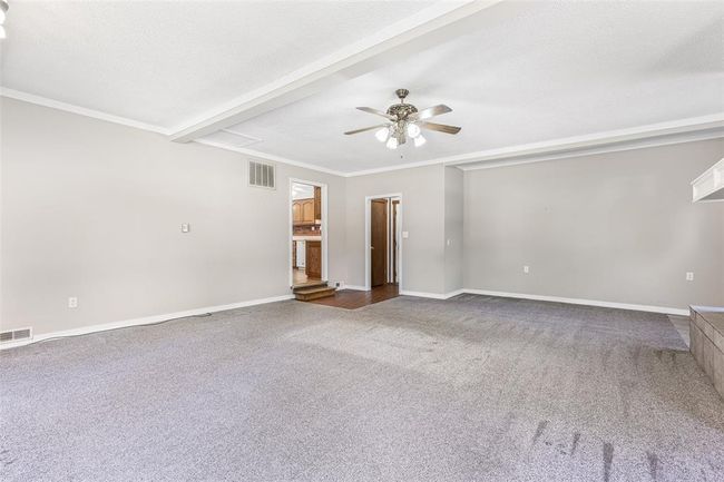 Spare room featuring ceiling fan, carpet floors, crown molding, baseboards, and beamed ceiling | Image 43