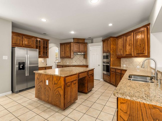 Kitchen with a sink, a center island, stainless steel appliances, arched walkways, and light tile patterned floors | Image 11