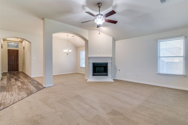 Unfurnished living room featuring lofted ceiling, arched walkways, carpet flooring, ceiling fan, and a chandelier | Image 7