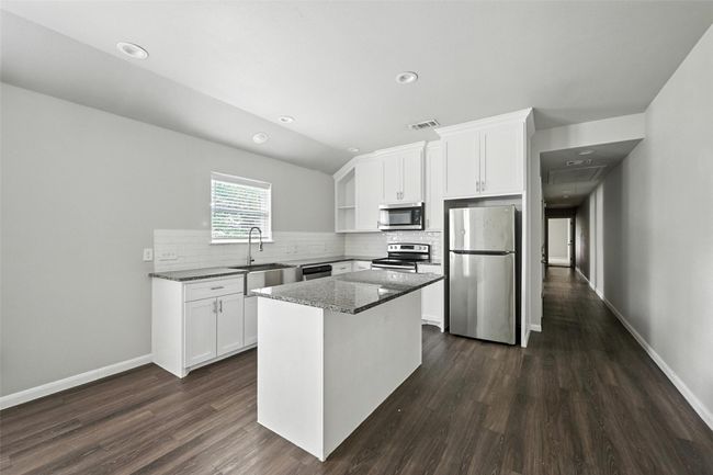 Kitchen with white cabinets, stainless steel appliances, dark stone counters, tasteful backsplash, and dark wood-style flooring | Image 6