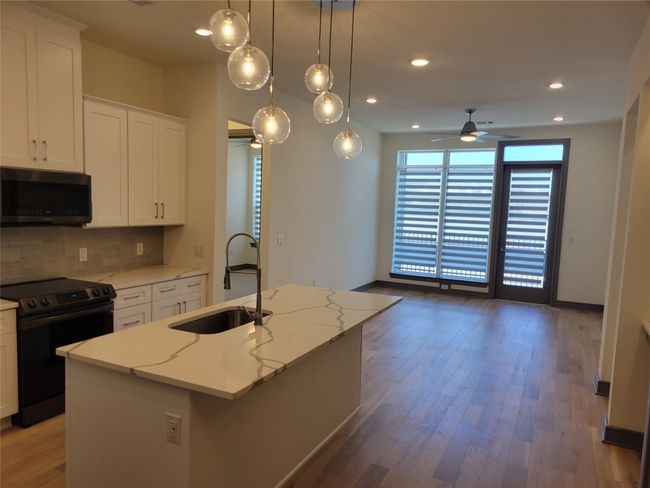 Kitchen featuring a sink, stainless steel microwave, tasteful backsplash, black range with electric stovetop, and an island with sink | Image 8