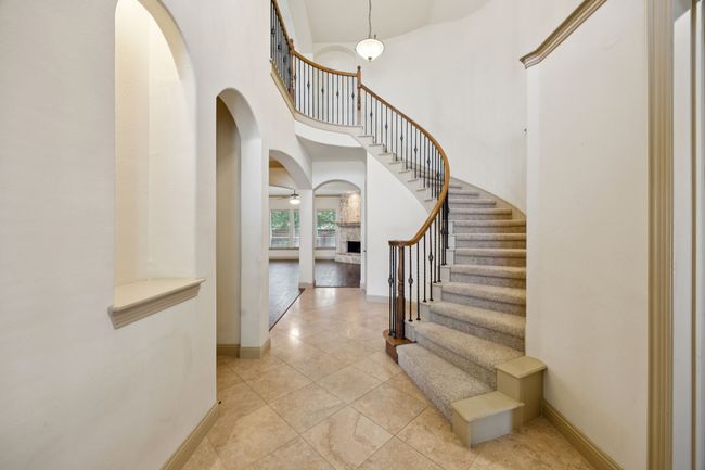 Foyer featuring arched walkways, baseboards, a towering ceiling, stairs, and light tile patterned flooring | Image 5