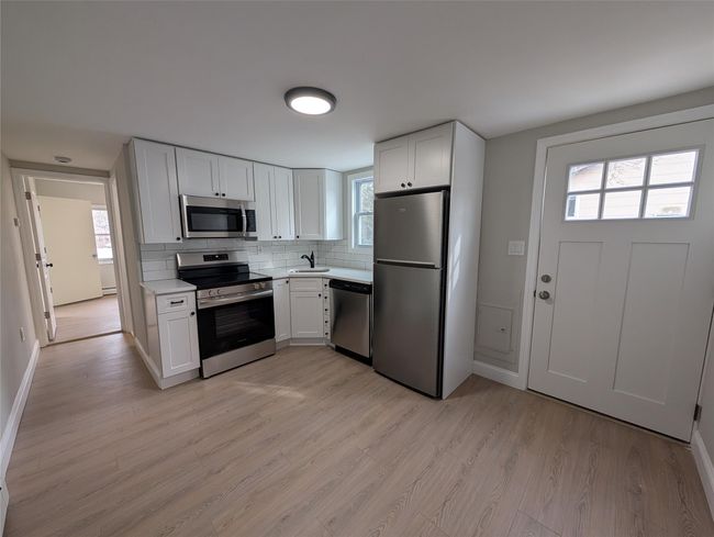 Kitchen featuring light wood-type flooring, a sink, backsplash, stainless steel appliances, and light countertops | Image 20