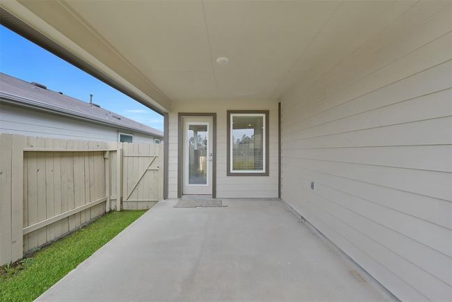 This photo shows a covered patio with concrete flooring, offering a cozy outdoor space. It features a wooden fence for privacy and a door leading into the house, perfect for relaxing or entertaining. | Image 22