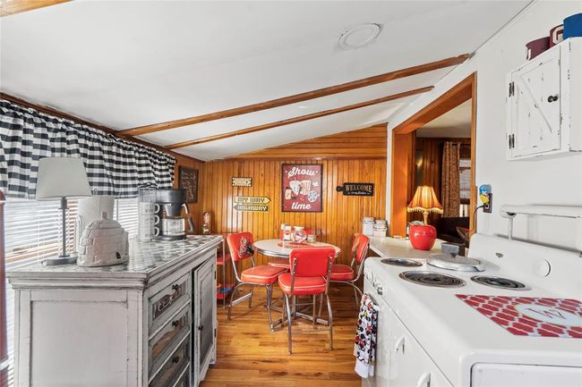 Kitchen with electric stove, white cabinetry, vaulted ceiling with beams, wooden walls, and light wood-type flooring | Image 12