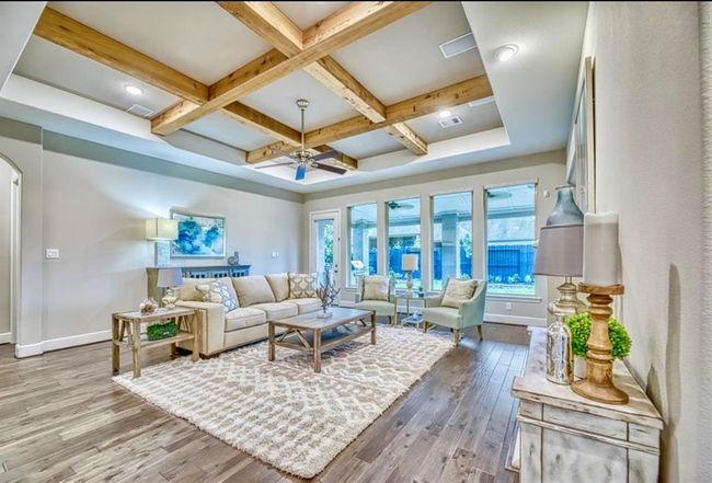 This spacious living room features a stylish coffered ceiling with wood beams, large windows offering plenty of natural light, and elegant hardwood flooring. The room is tastefully furnished with a cozy sofa, armchairs, and a decorative rug, creating a warm and inviting atmosphere. | Image 18