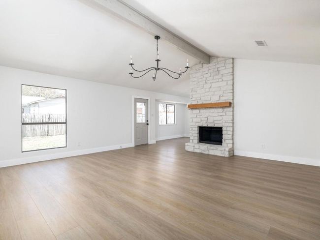 Unfurnished living room featuring baseboards, light wood-style flooring, vaulted ceiling with beams, and an inviting chandelier | Image 9