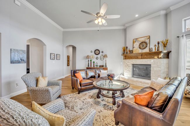 Living room with ceiling fan, light hardwood / wood-style floors, a stone fireplace, and ornamental molding | Image 7