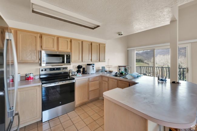 Kitchen with light countertops, a peninsula, stainless steel appliances, light brown cabinets, and light tile patterned floors | Image 8