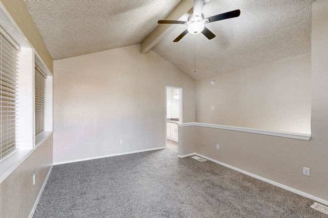 Carpeted spare room with a ceiling fan, visible vents, baseboards, lofted ceiling with beams, and a textured ceiling | Image 30