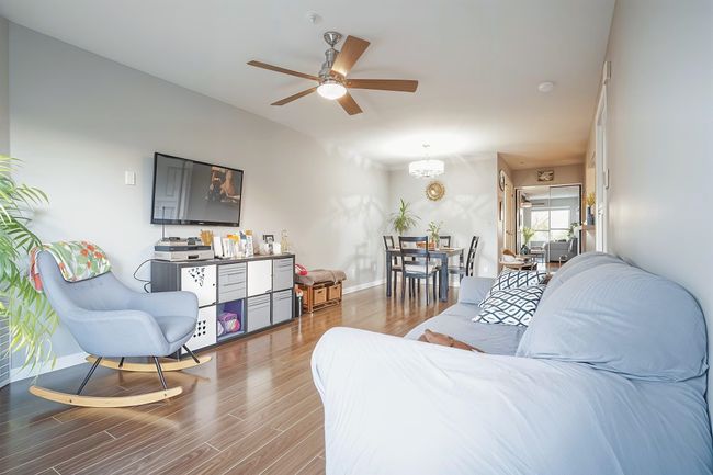Living area featuring ceiling fan with notable chandelier, wood finished floors, and baseboards | Image 7