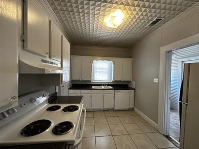 Kitchen with white range with electric cooktop, white cabinets, under cabinet range hood, light tile patterned floors, and crown molding | Image 7