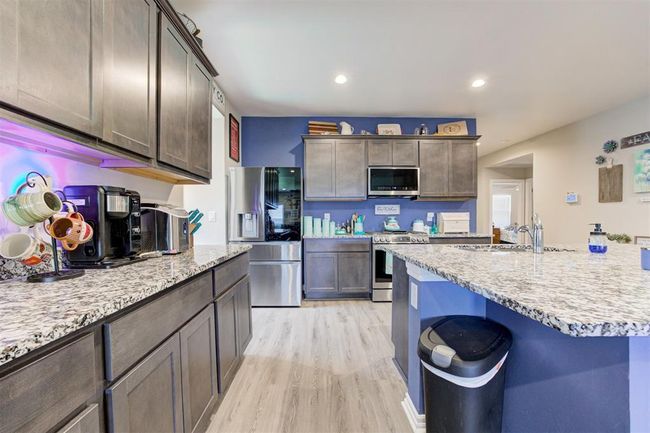 Kitchen featuring stainless steel appliances, light wood-type flooring, dark brown cabinetry, light stone counters, and recessed lighting | Image 13