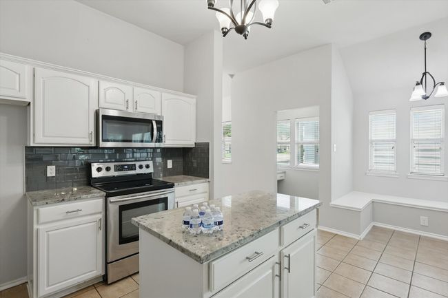 Kitchen featuring appliances with stainless steel finishes, a chandelier, tasteful backsplash, light stone countertops, and light tile patterned floors | Image 11