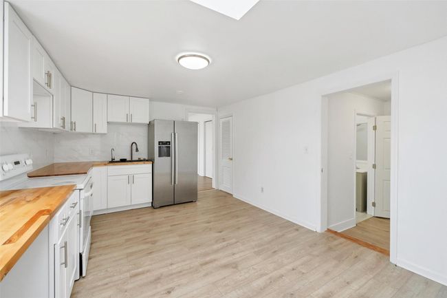 Kitchen with white cabinets, white electric range, wood counters, stainless steel fridge, and vinyl flooring | Image 6