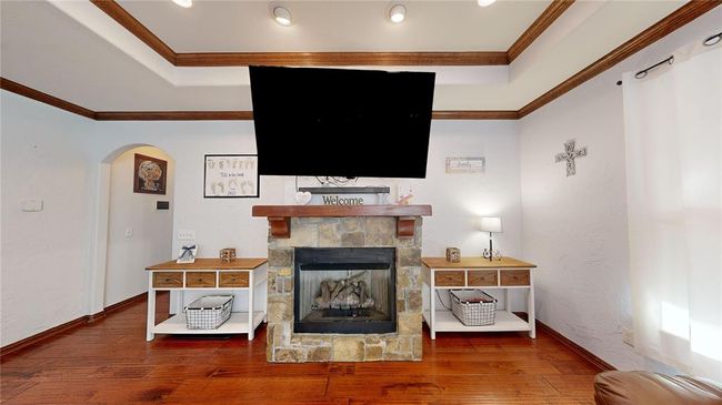 Living room with arched walkways, wood finished floors, crown molding, a stone fireplace, and a raised ceiling | Image 14
