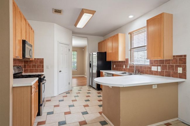 Kitchen featuring gas stove, a sink, a peninsula, decorative backsplash, and light countertops | Image 15