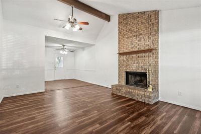 Unfurnished living room with vaulted ceiling with beams, ceiling fan, a brick fireplace, and wood-type flooring | Image 3